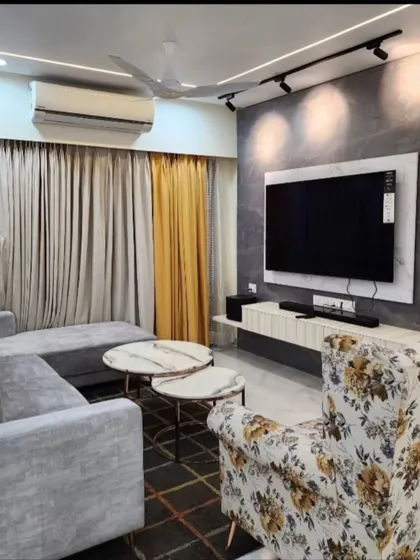 This view shows the living room setup with a grey sectional sofa and a floral accent chair. The combination of grey and yellow curtains adds a pop of color.