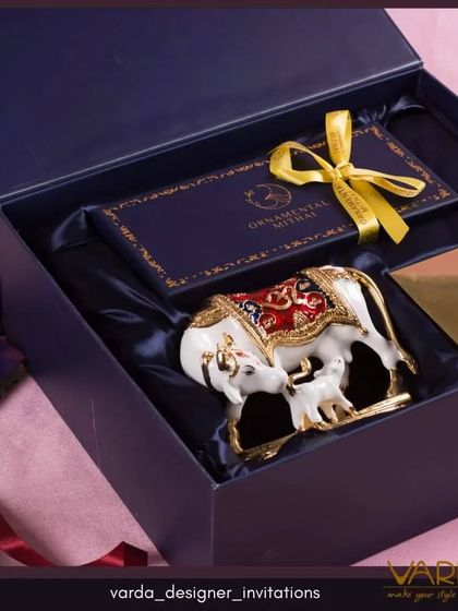 This luxurious gift hamper box is designed for a truly special announcement. The deep blue box is lined with satin and contains a beautifully crafted ornamental cow and calf figurine, symbolizing prosperity and auspicious beginnings.