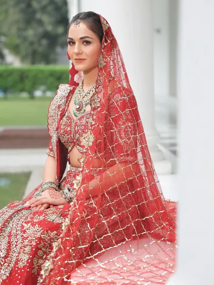 The sheer red veil adds a layer of mystery and tradition. The makeup underneath is kept soft and radiant, ensuring she glows from within.