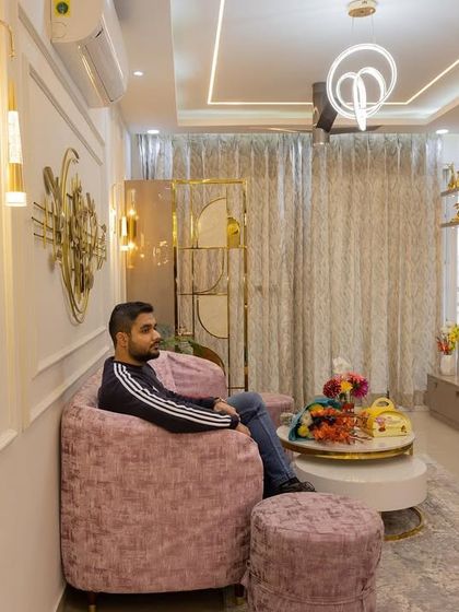 An inviting and magnificent living room at Eldeco Aamantran, featuring a plush pink sofa, elegant wall molding, and gold accents.