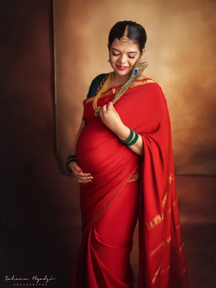 There is a unique power and grace in a traditional maternity portrait. This mom-to-be looks absolutely regal in a classic red silk saree, adorned with temple jewelry and a peacock feather, celebrating her journey with timeless elegance.