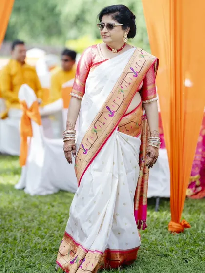 The mother of the bride looking chic and happy at the Haldi ceremony. Her look features a classic updo with a fresh flower, paired with simple makeup and cool sunglasses for the outdoor event.