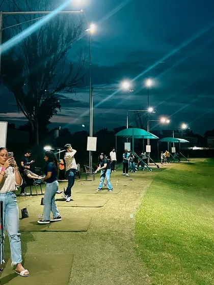 A perfect night for golf. A player captures a memory while her friends continue their practice under the lights.