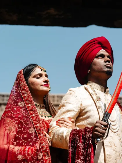 A regal portrait of the couple in traditional attire. The groom holds a sword, looking towards the future, while his bride stands by his side, creating a powerful image of partnership and strength.