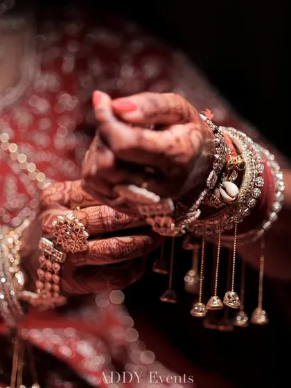 A close-up of the bride's hands, adorned with intricate henna and traditional kalire bangles, a symbol of her new journey.