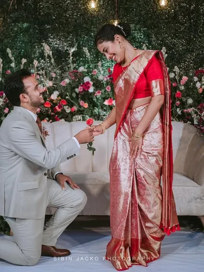 A beautiful moment captured as the groom proposes to his bride in front of a floral and greenery backdrop during their Calicut wedding.