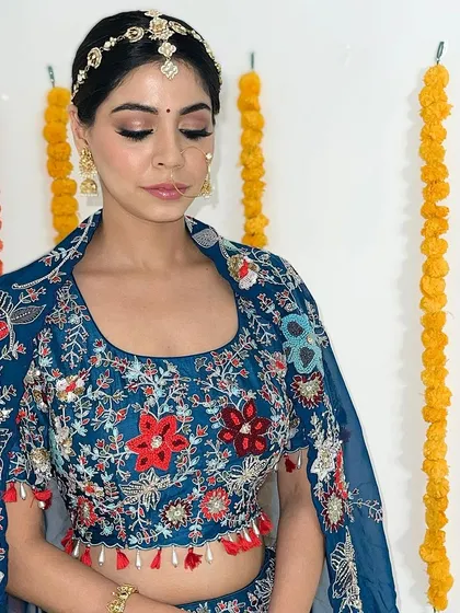 A beautiful look for a pre-wedding ceremony like a Mehendi or Sangeet. The makeup is fresh and glowing, with soft smokey eyes that complement the intricate embroidery of her blue outfit.