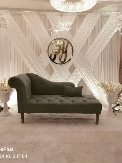 For a sophisticated engagement, we designed this all-white theme with crisscross draping, cherry blossom trees, and a custom neon sign. The elegant chaise lounge completes this clean, modern look for a banquet hall.
