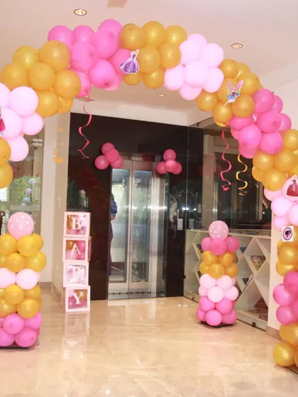 The entrance to a Barbie-themed party, with pink and gold balloons and 'BABY' blocks.