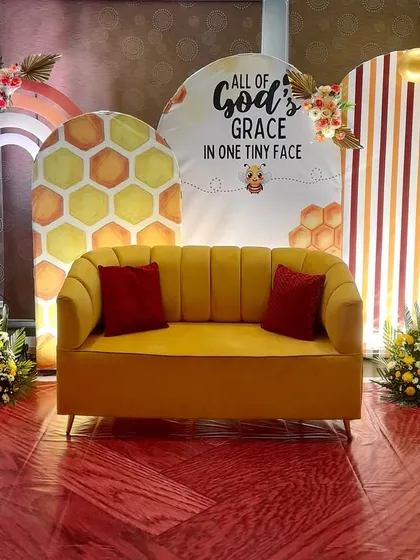 This cheerful and modern baby shower setup uses a 'sweet as can bee' honeycomb theme. We designed custom arched backdrops with warm stripes and honeycomb patterns, complemented by a vibrant yellow balloon arch and a comfortable sofa for the parents-to-be.