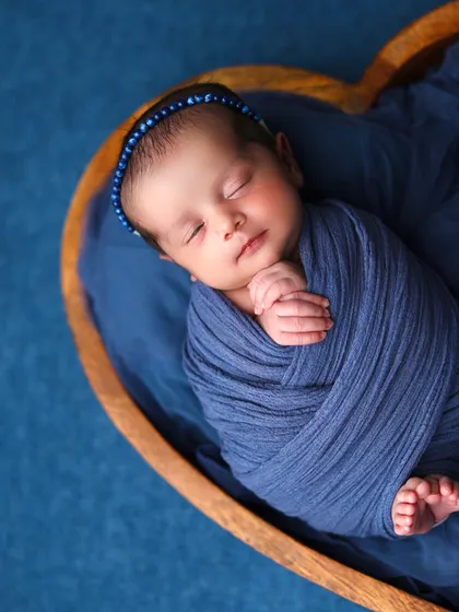 A close-up portrait of the baby in the blue heart bowl, focusing on the calm expression and tiny, folded hands.