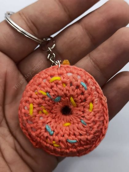 A close-up of my handmade crochet donut keychain held in my hand. You can see the detail of the stitches and the colorful sprinkles.