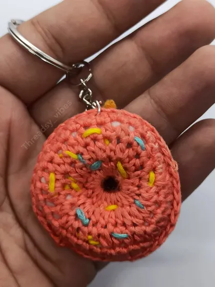 A close-up of my handmade crochet donut keychain held in my hand. You can see the detail of the stitches and the colorful sprinkles.