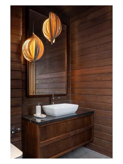 A bathroom vanity with dark wood paneling and sculptural pendant lights. The design demonstrates how we use rich materials and thoughtful lighting to create a warm and elegant atmosphere.