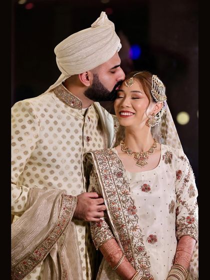 A happy portrait of a newlywed couple. The groom's affectionate kiss on the bride's forehead and her joyful smile make for a perfect wedding photograph.