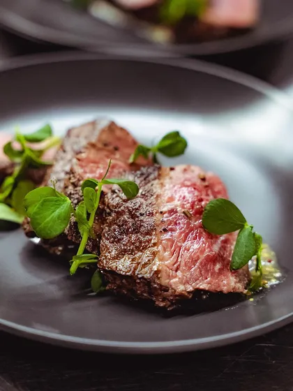 A perfectly cooked steak, sliced to reveal a beautiful medium-rare interior. This dish showcases our versatility and skill with wood-fired cooking beyond pizza.