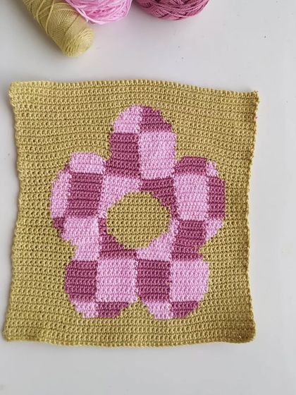 This checkered flower square is an example of tapestry crochet. This technique allows for creating detailed, graphic images with yarn, perfect for wall hangings or pillows.