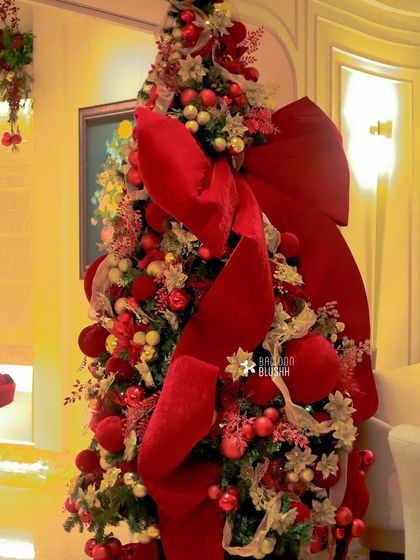 Another angle of the grand Christmas tree, showing the oversized red velvet ribbon cascading down its sides.