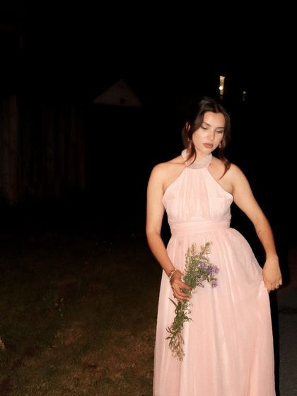 A full-length shot of the pink dress, holding a bouquet of wildflowers.