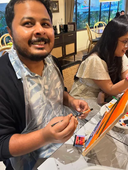 A participant wearing a protective apron smiles as he works on his painting, fully enjoying the creative process.