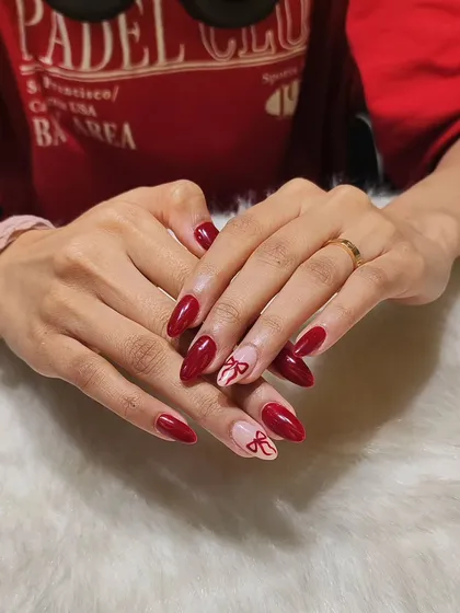 Simple, elegant, and cute. This set features glossy red almond nails with two sheer accent nails decorated with a delicate, hand-painted red bow.