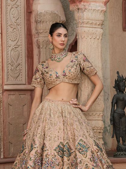 A full-length shot of the model in the beige lehenga and navratan choker, standing next to a traditional statue, blending modern style with heritage.