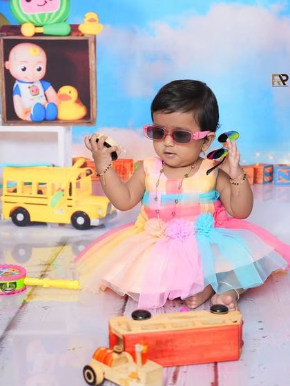 A cool baby girl in a rainbow dress and sunglasses plays with toys in a Cocomelon-themed setup. This shot is full of color, fun, and personality.