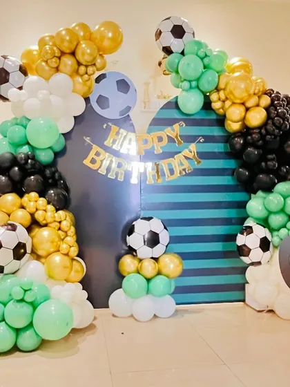 For the ultimate football fan, we transformed this space into a mini stadium. This football-themed birthday decoration includes balloon arches in green, black, white, and chrome gold, along with multiple football-themed foil balloons. A custom striped backdrop and a "GO" cutout add to the sporty atmosphere.