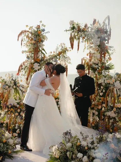"You may now kiss the bride." A classic, emotional moment from a beautiful Christian wedding, captured as the couple seals their vows amidst stunning floral arrangements and the beauty of the hills.