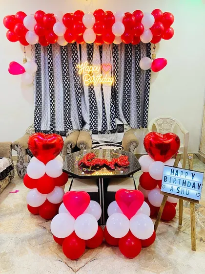 A romantic red and white themed birthday decoration for an intimate home celebration, featuring heart-shaped balloons and a personalized light box.