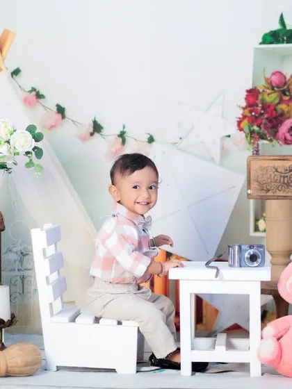A one-year-old boy looking dapper in a checkered shirt, sitting at a desk in our bright and airy boho-themed setup.