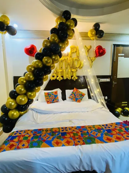 A stylish birthday room setup featuring a diagonal black and gold balloon garland over a fairy light canopy.