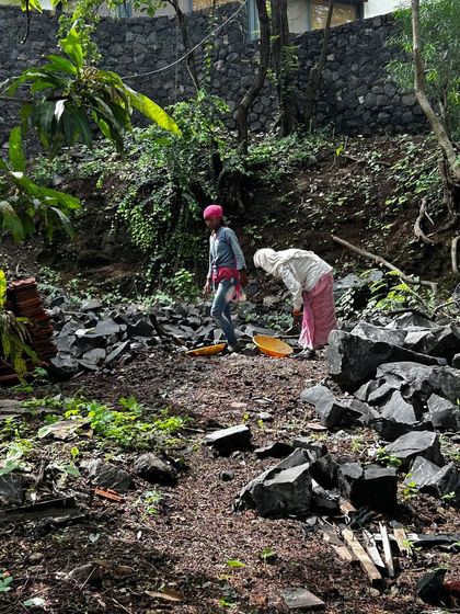 Workers clear a sloped site in Alibaug, sorting through salvaged materials and preparing the ground for construction. This initial phase is vital for understanding the landscape and planning our approach.