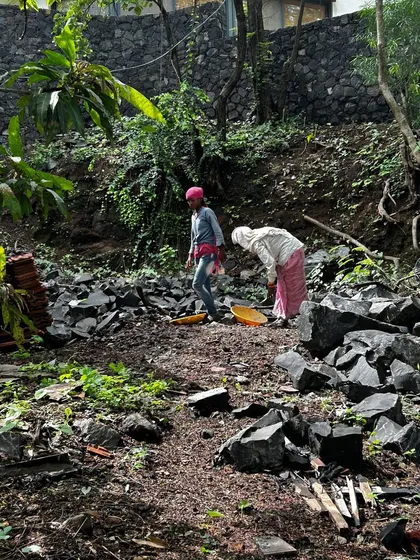 Workers clear a sloped site in Alibaug, sorting through salvaged materials and preparing the ground for construction. This initial phase is vital for understanding the landscape and planning our approach.