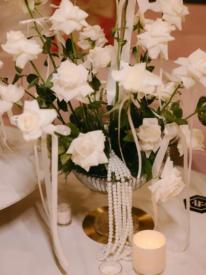 A classic centerpiece of white roses, adorned with delicate ribbons and a string of pearls.