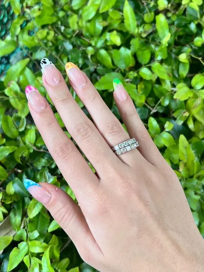A playful and eclectic French manicure with each tip featuring a different colorful animal print design on long, clear extensions.