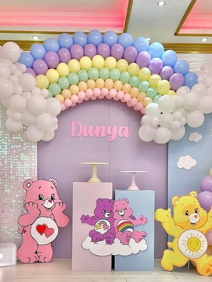 A wider view of the Care Bears and rainbow party setup, showing the full backdrop, a light-up number '1', and a sequin panel.