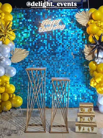 For a touch of glamour, we designed this stunning birthday backdrop. It features a vibrant blue shimmer wall that catches the light beautifully, framed by bold yellow and silver balloon garlands and a bright "Happy Birthday" neon sign.