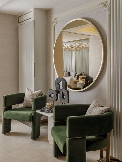 A detail of the foyer, where a sculptural green chair sits beside a marble side table and a large mirror that reflects the living space beyond.
