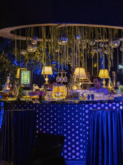 A quirky and stylish circular bar with a polka-dot front, adorned with hanging disco balls and classic table lamps for a unique party vibe.