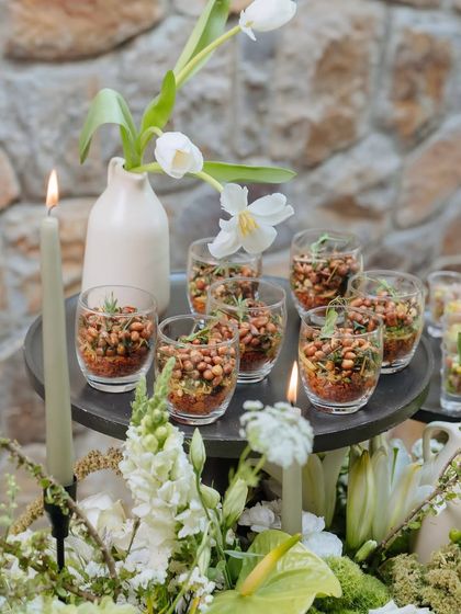 A close-up of appetizers served in glasses on the Earth Table. The food is nestled among candles and white tulips, making every dish part of the decor.
