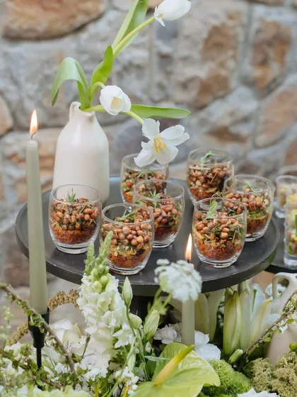 A close-up of appetizers served in glasses on the Earth Table. The food is nestled among candles and white tulips, making every dish part of the decor.