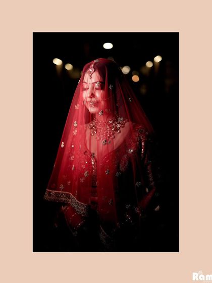 A soft and dreamy portrait of the bride under her red veil, with a dark background making her glow.