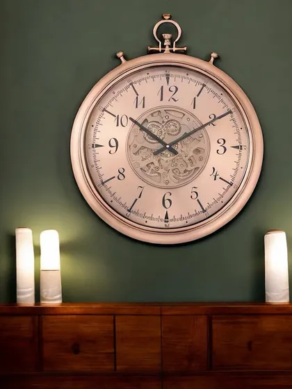 A large, elegant wall clock in a rose gold finish. The classic numerals and central moving gears make it a sophisticated timepiece that blends seamlessly with luxurious interiors.