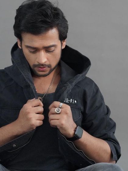 A thoughtful, seated studio portrait. The model adjusting his jacket creates a natural, candid feel within a controlled studio environment.