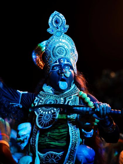 An artist's striking portrayal of the goddess, captured at night. The vibrant blue makeup and intricate costume stand out dramatically against the dark background.