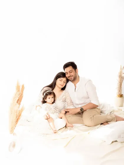 A serene family portrait where the parents and their young daughter cuddle together on a soft white blanket. The image conveys a sense of peace, comfort, and love.