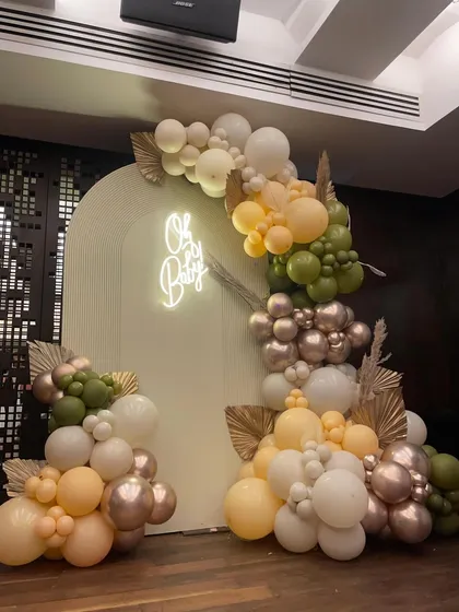 An elegant baby shower setup featuring an 'Oh Baby' neon sign and a beautiful organic balloon arch in earthy tones of olive green, peach, and metallic rose gold.