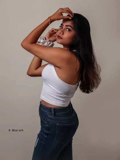 A clean and simple studio portrait of a model in a white ribbed tank top and blue jeans. The plain background puts all the focus on the classic, timeless outfit.
