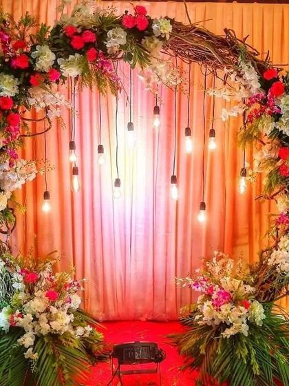 A rustic-chic circular arch made of twigs and decorated with colourful flowers. Hanging Edison bulbs add an industrial and warm touch, making it a perfect backdrop for a trendy engagement or sangeet.
